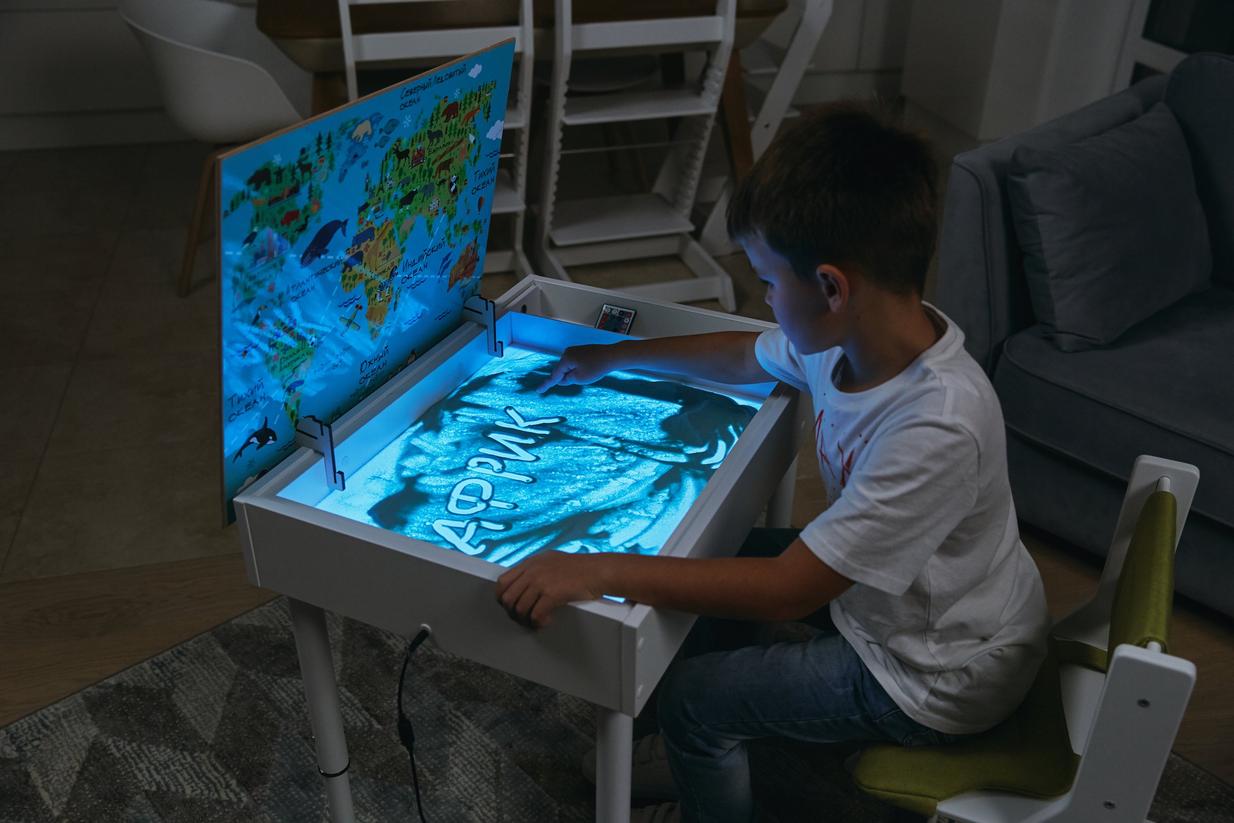Ребенок рисует на светящемся песке в световом столе MYPLAYROOM, рядом карта мира